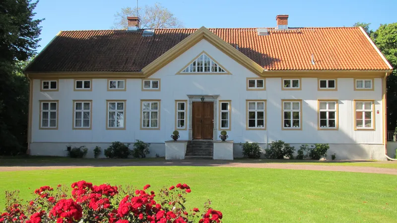 Vit herrgårdsbyggnad med rött tegeltak och röda rosor i förgrunden