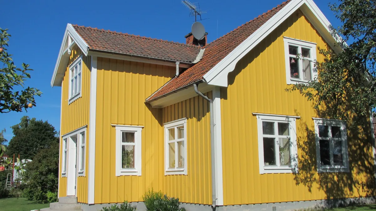 Gult tvåvåningshus i trä med vita knutar och fönster